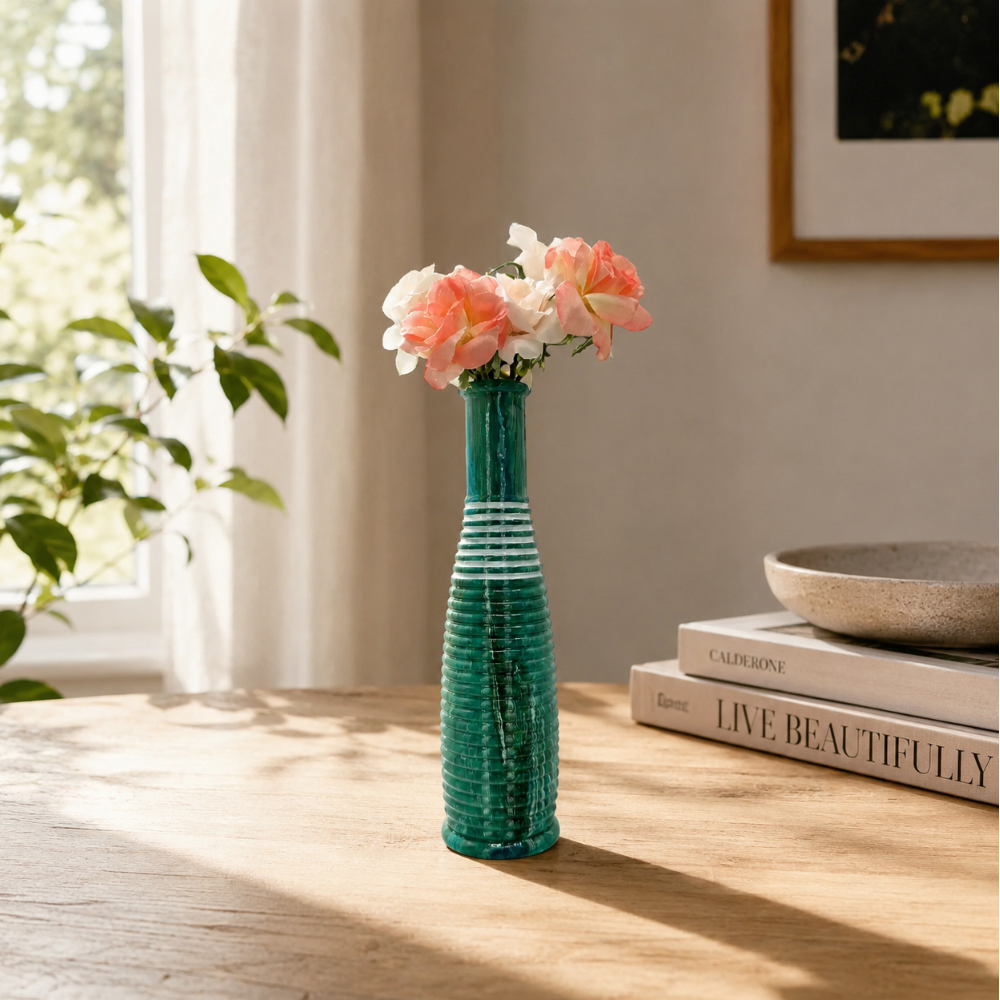 Green vase with flowers on a wooden table near a window