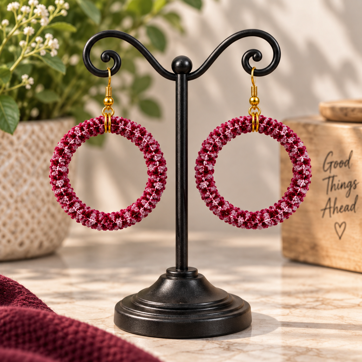 Handmade wool-wrapped hoop earrings with soft wool fibers in burgundy, raspberry, and blush pink displayed on an earring stand.