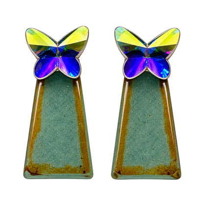 a faceted silver-colored butterfly catching the light and reflecting back blues and yellows, with a teal-green geometric drop accented with warm golden tones